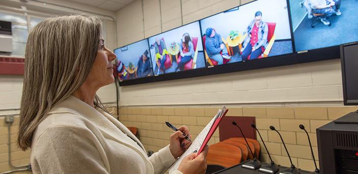 Dr. Christy Lyons Graham watching students' practice counseling sessions on a row of TV monitors and taking notes